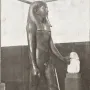 Statue of King Hor standing in a museum display, wearing a striped headdress and false beard and holding a staff.