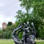 Monument to Dog Jock bronze sculpture of a small dog cradled in large human hands on a stone pedestal in a park.