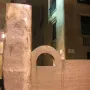 Topos V sculpture by Chillida with a tall pillar and an arched block against historic stone buildings.