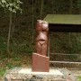 Venus of Petrkovice sculpture on an inscribed plinth and stone-filled gabion base in a wooded setting.