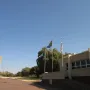 The National Women\'s Monument stands on a raised base in a grassy landscape with a paved path leading toward it and a modern building nearby.