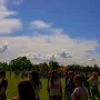 The Endless Column rises beside a green field under a blue sky with clouds, with many people gathered below.
