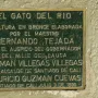 Green commemorative plaque with raised metal lettering mounted on a textured wall.