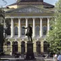 Pushkin statue stands before the Mikhailovsky Palace with a classical facade and trees in the background.