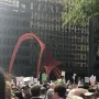 Flamingo sculpture in red steel rising above a crowd in front of a dark building with reflective windows.