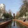El Llarg Viatge at the end of a long reflecting pool, with trees, buildings, and people mirrored in the water.