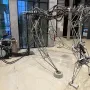 The Senster robotic sculpture with a skeletal metal framework, cables, and jointed limbs beside a separate machinery unit.
