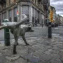 Het Zinneke bronze dog sculpture lifting its leg beside a street bollard in Brussels.