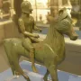 Armento Rider bronze statuette of a helmeted rider on a horse, shown on a clear stand.