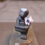 Järnpojke sculpture with a shiny head, a small flower in its chest, and coins scattered in front