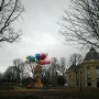 Bouquet of Tulips sculpture with a hand holding pink, yellow, and red tulips against bare tree branches and an overcast sky.