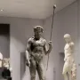 Tiber Dionysus bronze statue of a standing nude male figure with a wreath and staff in a museum.