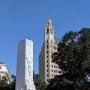 The Alamo Cenotaph stands in front of the Morgan Hotel tower under a clear blue sky.