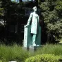 Lincoln the Lawyer bronze statue of Abraham Lincoln standing outdoors on a pedestal with evergreen trees behind it.