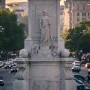 Peace Monument rising in the middle of a busy tree-lined avenue with American flags and cars nearby.