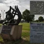 Monument to Dog Jock bronze sculpture of a small dog cradled in large human hands on a stone pedestal in a park.