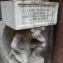 Il Gobbo di Rialto, a weathered stone figure crouching beneath an inscribed block beside a reddish column.