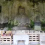 Usuki Stone Buddhas carved into a rock face, with a central seated figure and smaller figures nearby beside offerings and a wooden fence