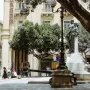 Great Siege Monument with three bronze draped figures on a white base beside a street lamp and cannon.
