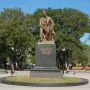 The Chekhov monument shows a bronze seated figure holding a book on a dark granite pedestal in a park.