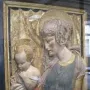 Painted terracotta Madonna and Child relief in a dark frame behind reflective glass.