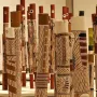 Decorated hollow log tombs from the Aboriginal Memorial stand upright in a dense group, painted with stripes, zigzags, and stylized figures.