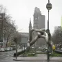 Light-grey tubular sculpture by Brigitte und Martin Matschinsky-Denninghoff in a city plaza, with a historic church ruin in the background.