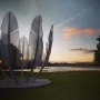 Kindred Spirits sculpture with curved metallic feather-like forms beside the water at sunset.