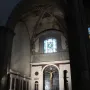 Brunelleschi Crucifix mounted on a dark cross beneath a marble archway, with two visitors in the foreground.