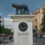 Capitoline Wolf sculpture of a she-wolf suckling two infants on a tall stone pedestal.