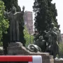 Bronze Monument to Saint Francis of Assisi with robed figures on a stepped stone plinth under a blue sky.