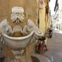 Fontana dello Sprone, a white marble fountain with a grotesque bearded face and conch-shaped basin built into a corner wall.