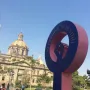 Antimonumenta sculpture shaped like the female gender symbol with a raised fist, set against a cathedral and blue sky.