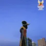Dona i Ocell sculpture with colorful mosaic tiles and a tall vertical opening against a twilight city skyline.