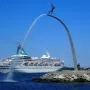The God our Father on the Rainbow sculpture beside a white cruise ship passing on the water.