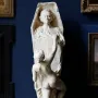 La Gloire sculpture showing a nude female figure pulling boards away from a coffin-shaped structure, revealing a male bust inside.