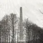 The Needle, a tall stone monument on a tiered base in a grassy clearing with bare trees behind it.