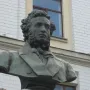 Pushkin bust on a tall pedestal in a paved plaza before a grand columned building.