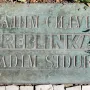 Weathered bronze Treblinka memorial plaque with carved Cyrillic and Latin text set into the ground.