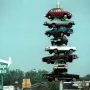 The Spindle sculpture with eight cars stacked vertically on a central pole above a shopping center sign.