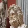 Marble bust of Zeus of Otricoli with a bearded face and curly hair, displayed on a pedestal in a museum gallery.