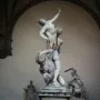 The Rape of the Sabine Women marble sculpture shows three intertwined figures in a dynamic pose inside an arched loggia.