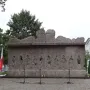 The Monument to Victims of the Wola Massacre, a rugged granite memorial with abstract human figures and circular recesses on its facade.