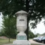 The Cuban Friendship Urn on a tiered stone pedestal with a bronze plaque, standing in a grassy park near a path and trees.
