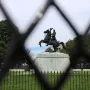 Andrew Jackson statue on a rearing horse, seen through a blurred fence with trees and buildings in the background.