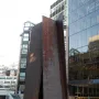 Fulcrum, a large rusty metal sculpture with leaning panels forming a triangular opening in an urban plaza.