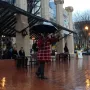 Allow Me sculpture of a figure in a checkered coat holding an open umbrella on a wet brick plaza.