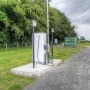 Electric vehicle charging station beside a gravel path at Northumberlandia, with trees, grass, and a utility box behind it.