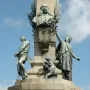 Upper section of the Rius i Taulet Monument with a bronze bust on an obelisk, flanked by bronze figures and a small putto holding a branch.
