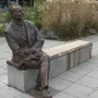 Willy Brandt Memorial bronze statue of a seated man in a suit on a bench, with tall dry grasses behind it.